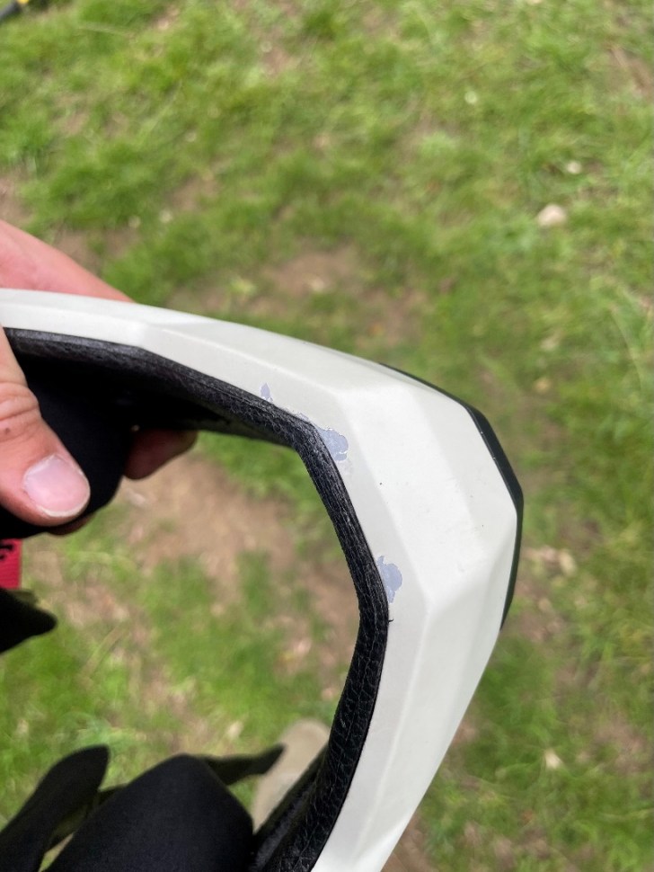 Close-up view of the edge of a Sweet Protection Fixer helmet showing paint chips on the chin guard, with a blurred background of grass.