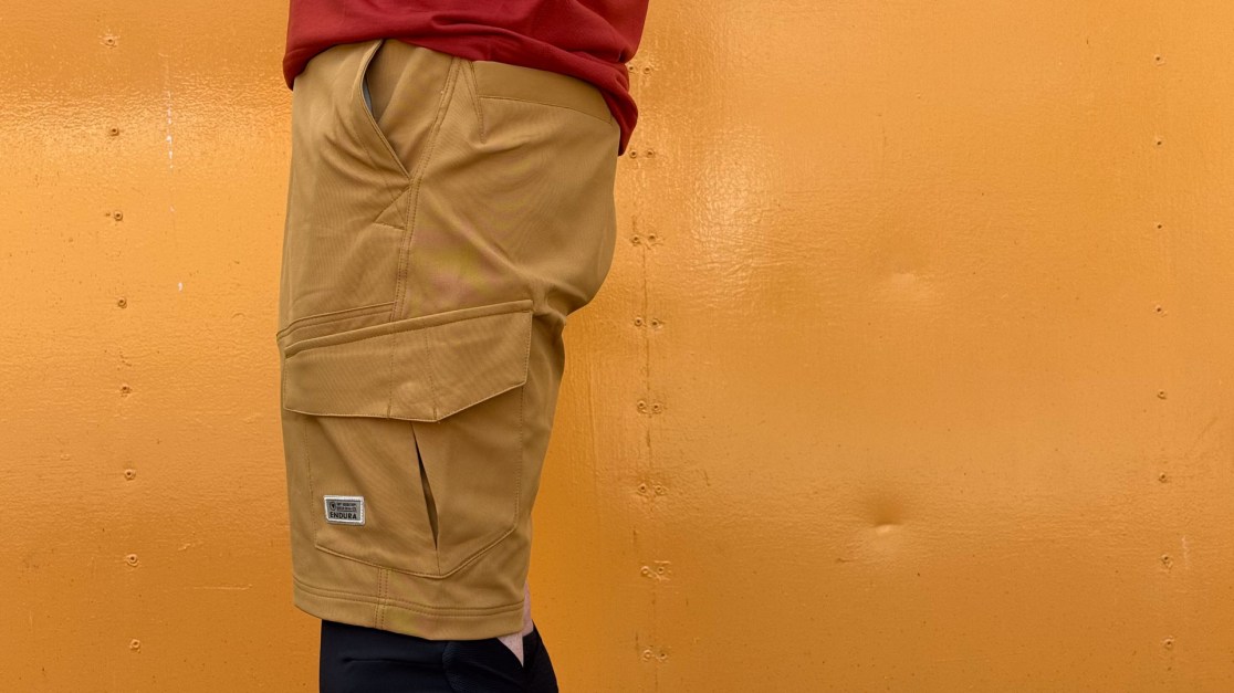 A close-up of a person wearing tan cargo shorts, with an orange background.