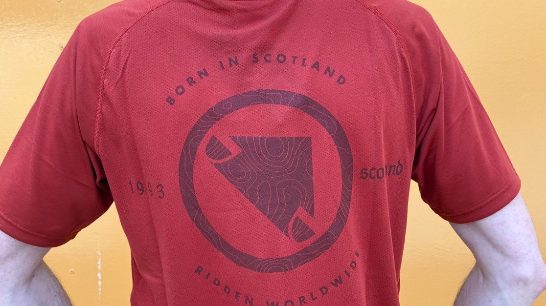 Back view of a person wearing a red t-shirt featuring the text 'Born in Scotland', the year '1993', and the phrase 'RIDDEN WORLDWIDE' along with a graphic design.