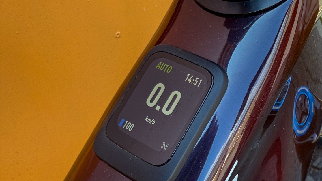 Close-up view of a digital display on a bicycle, showing a speed of 0 km/h and a battery level indicator, against an orange background.