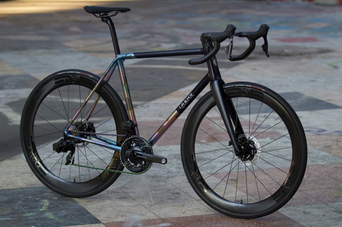 A custom road bike with a glossy multicolored paint finish, featuring sleek aerodynamic design and high-performance components, displayed against a patterned surface.