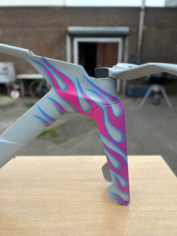 Close-up of a bicycle frame with a grey paint finish featuring vibrant pink and blue flame designs.
