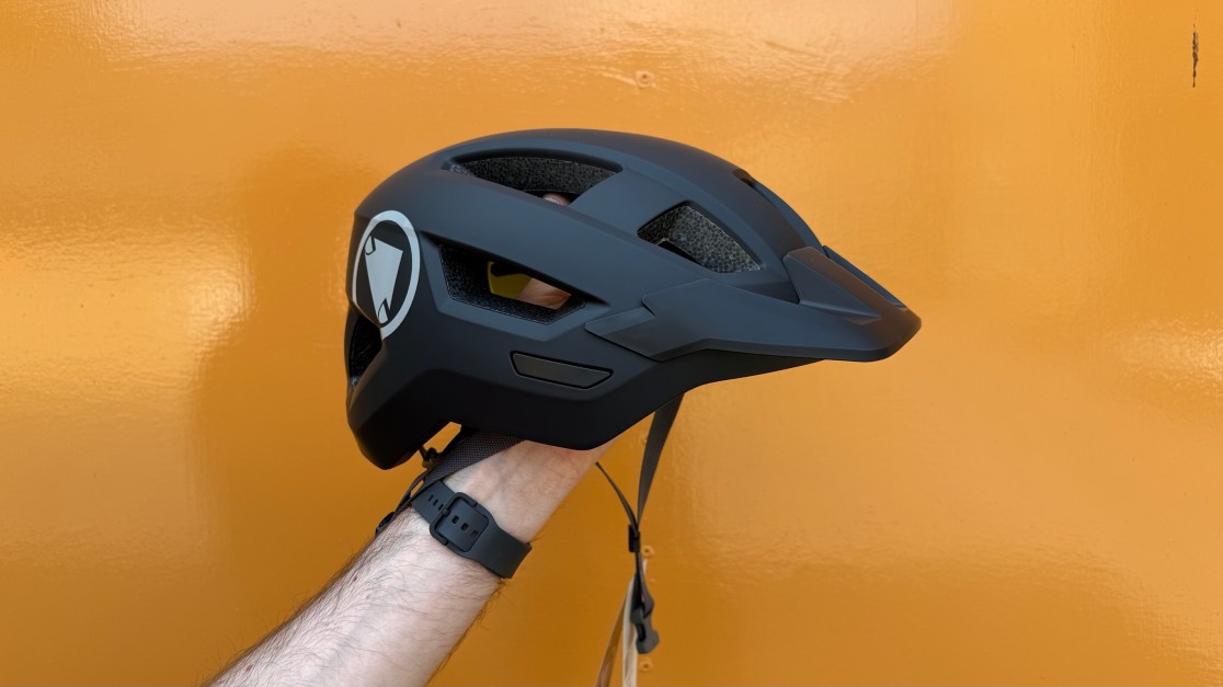 A black cycling helmet being held against an orange background.