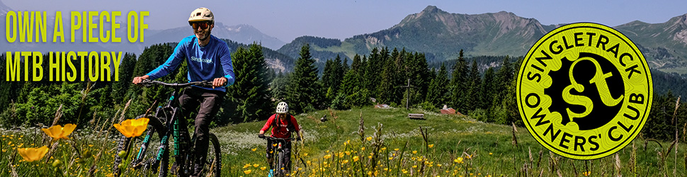 A scenic mountain biking trail with two riders navigating through a field of wildflowers, featuring mountains in the background and a logo for Singletrack Owners' Club.