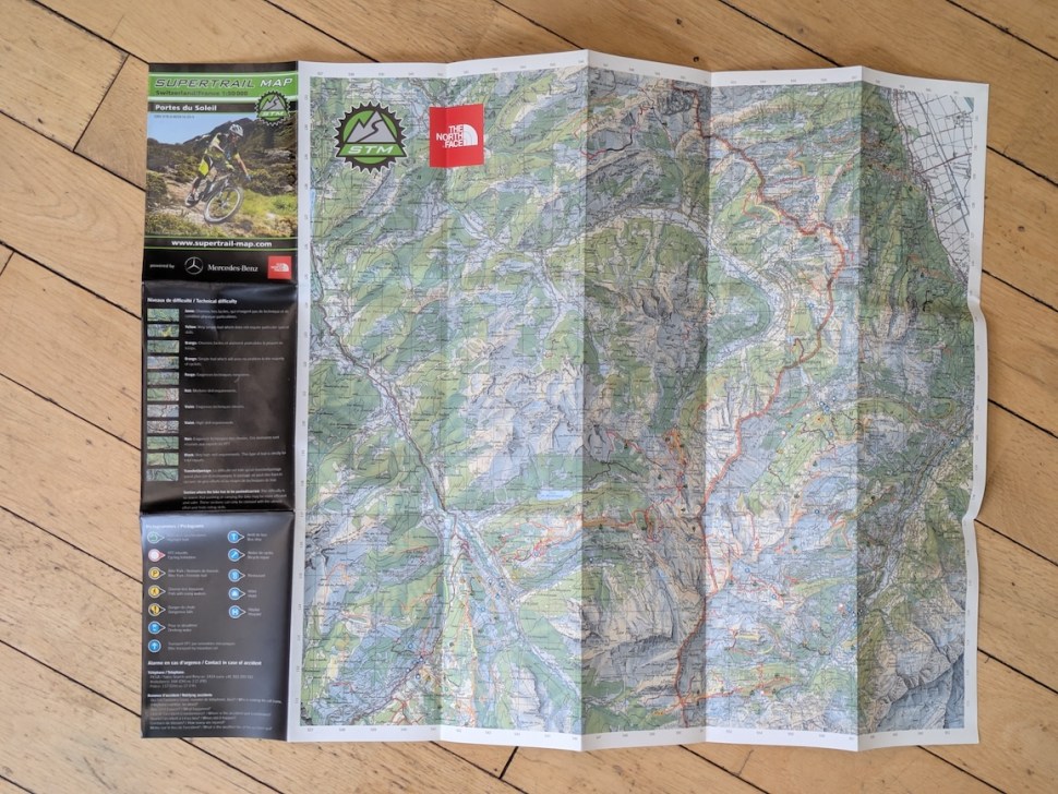 A folded map of the Portes du Soleil region, featuring highlighted trails and paths for biking, along with branding from Supertrail Map and The North Face.