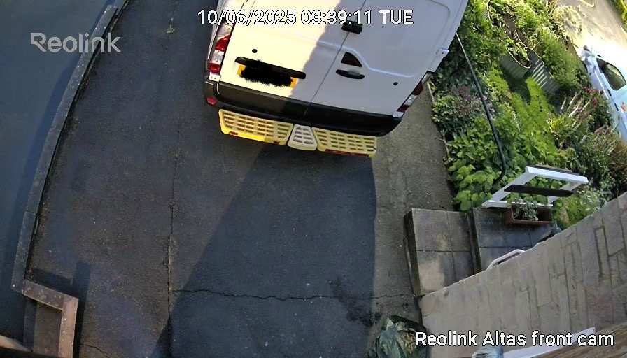View from Reolink Altas security camera showing a white van parked on a driveway during early morning hours, with surrounding garden and pathway details.