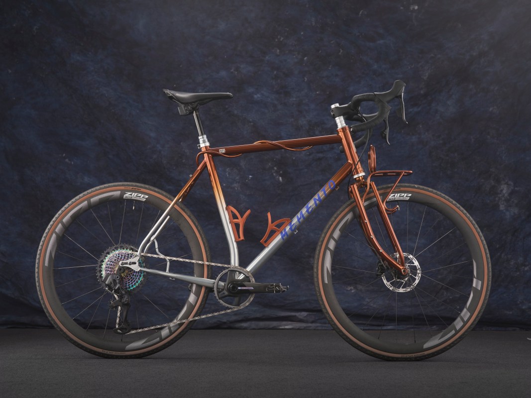 A custom bicycle with an orange and silver frame, showcasing intricate craftsmanship, set against a dark blue backdrop.