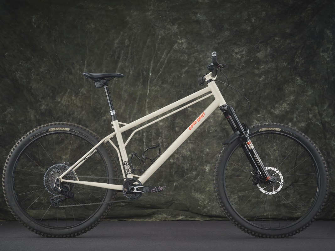A close-up side view of a modern mountain bike with a beige frame, black components, and the words 'GOOD GRIEF' prominently displayed.