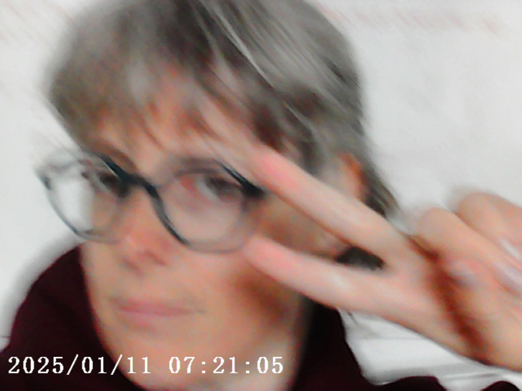 A blurred selfie of a person making a peace sign while wearing glasses, with a timestamp at the bottom.