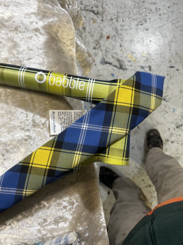 A close-up of a plaid tie in blue and yellow lying on a flat surface next to a multi-colored bike frame and a tag with care instructions.