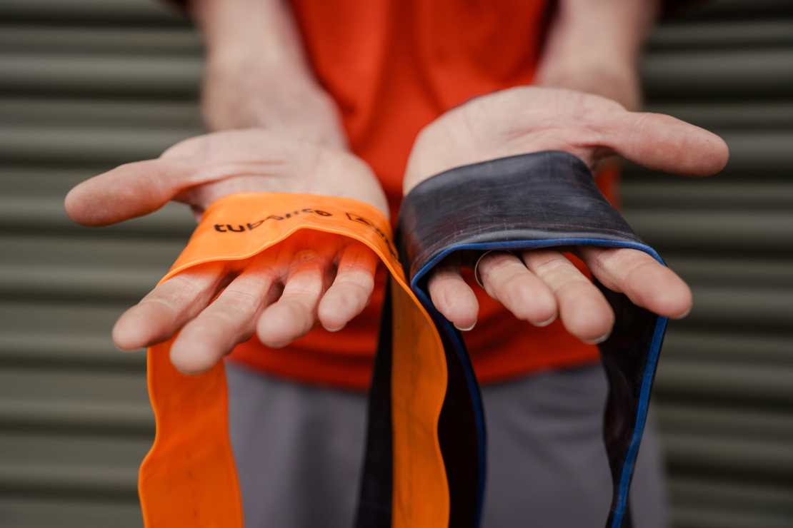 A person holding two bicycle inner tubes in their hands, one orange Tubolito tube and one black butyl tube, showcasing size and material differences.