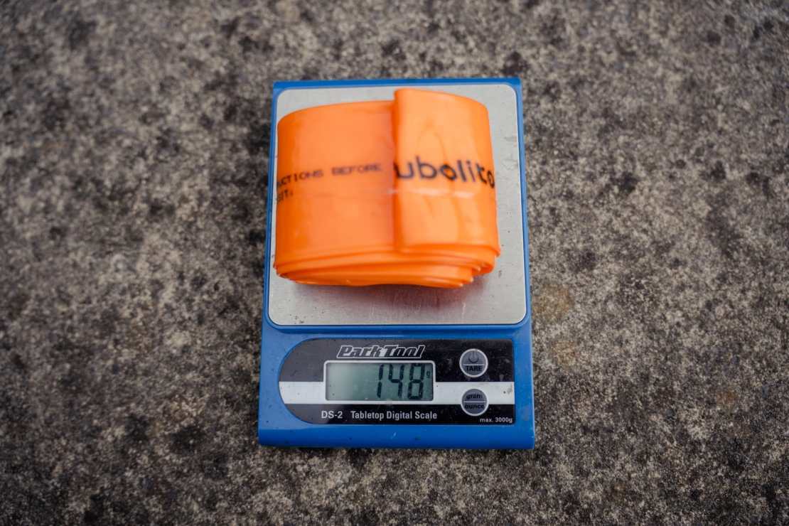 A bright orange Tubolito tube placed on a digital scale displaying a weight of 148 grams.