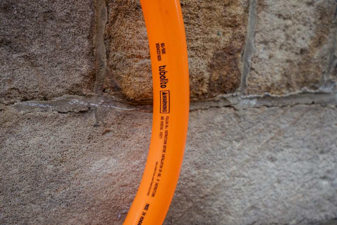 Close-up of a bright orange Tubolito tube against a textured stone wall, displaying warning instructions and branding details.