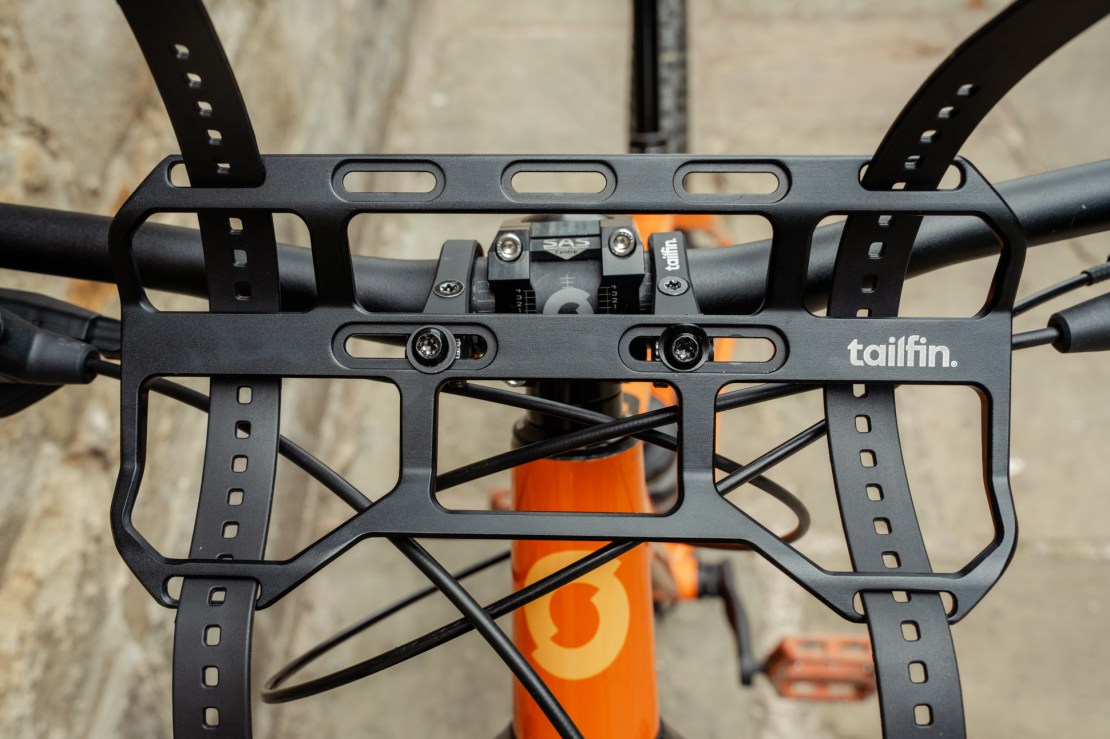 Close-up view of a Tailfin bar cage attachment system mounted on a bike handlebar, showcasing its adjustable straps and sturdy design.