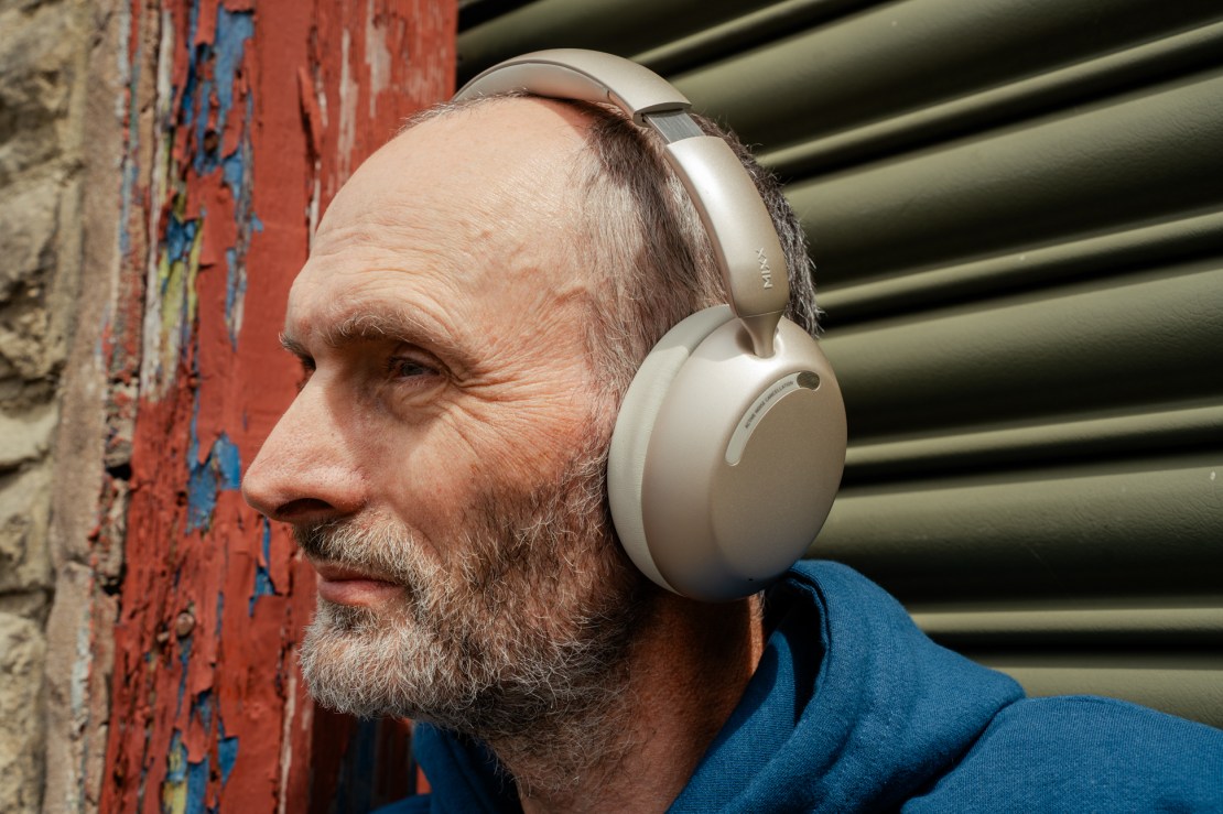 A close-up portrait of a man wearing soft over-ear headphones, showcasing a side profile against a textured wall.
