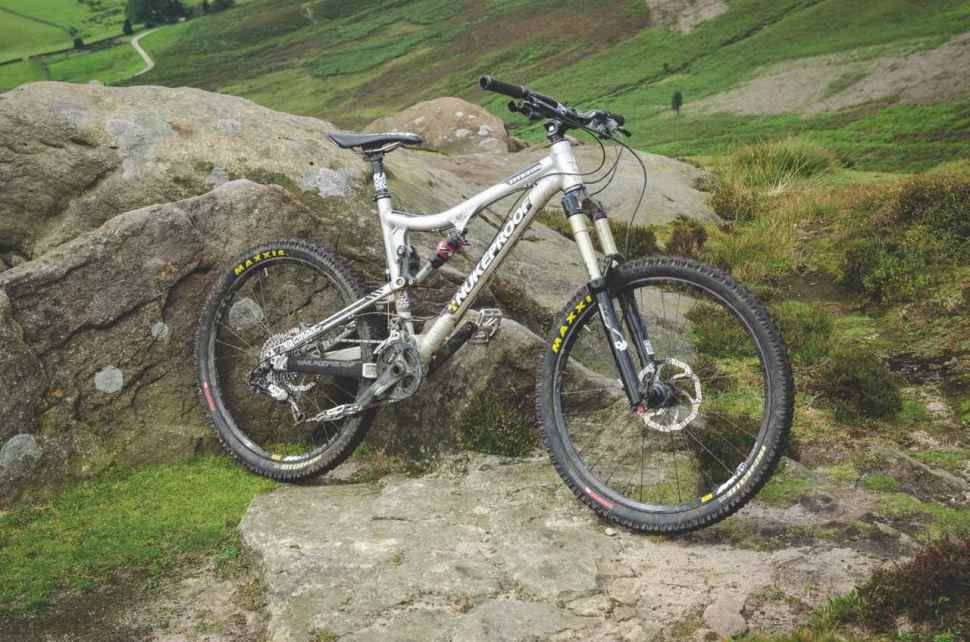 A Nukeproof mountain bike resting on a rock in a scenic green landscape.