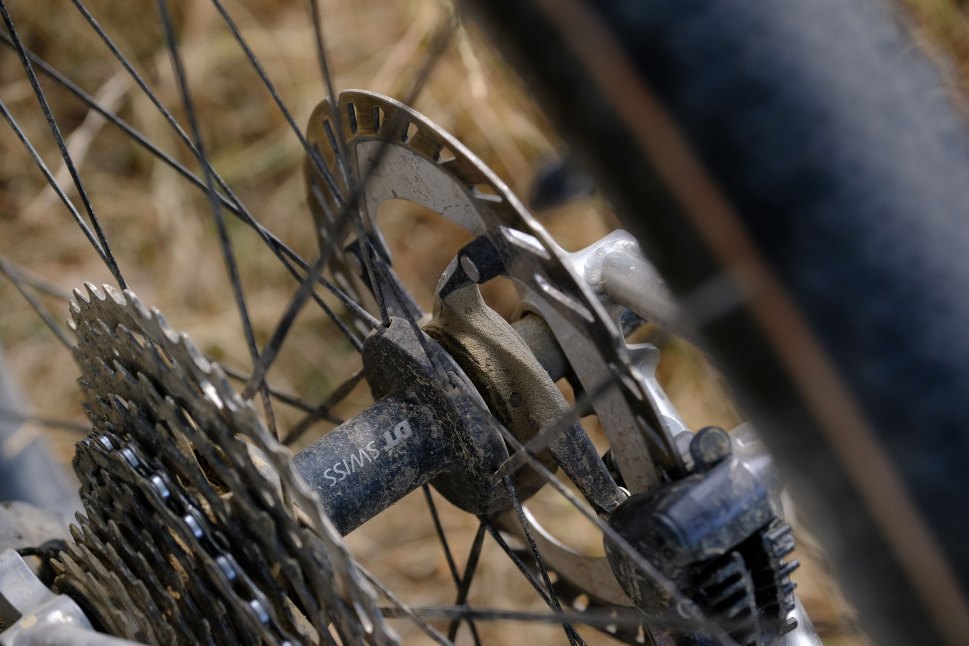 Close-up of a bicycle's rear cassette and disc brake, showcasing the DT Swiss branding and dirt accumulation.