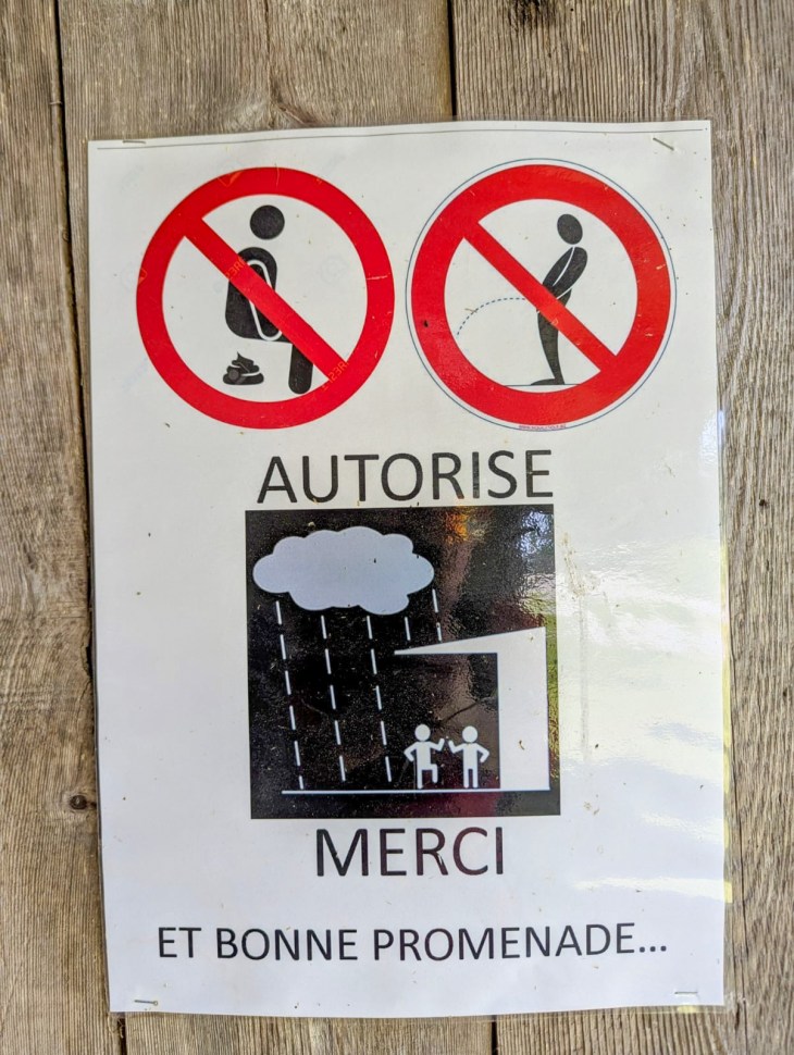 A sign in French with illustrations indicating that urinating and defecating are prohibited in the area, with a message wishing a good walk and a depiction of rain.