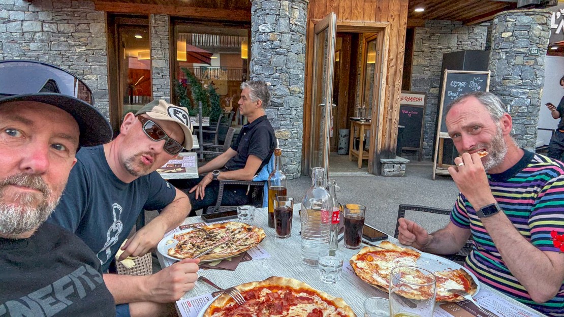 Men enjoying pizza at an outdoor restaurant in Les Gets, France.