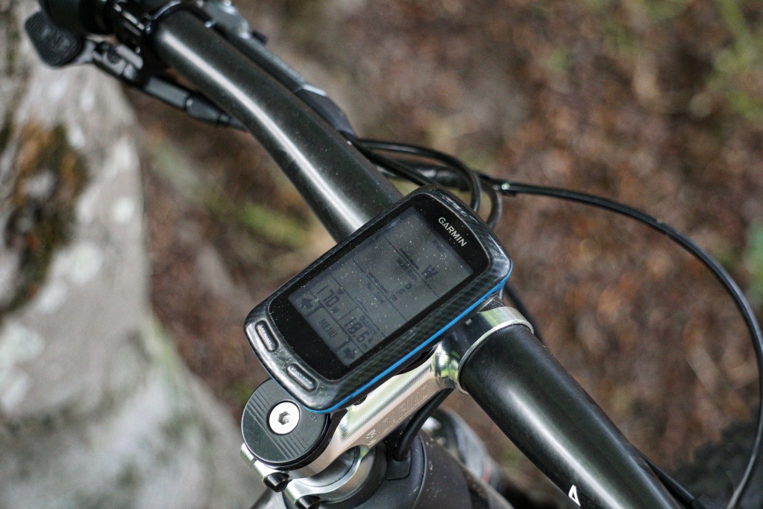 A close-up view of a Garmin bike computer mounted on a mountain bike's handlebar, showing data metrics such as speed and power.
