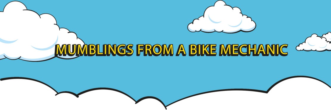 A graphic featuring the title 'Mumblings From A Bike Mechanic' in bold yellow letters against a light blue sky background with white clouds.