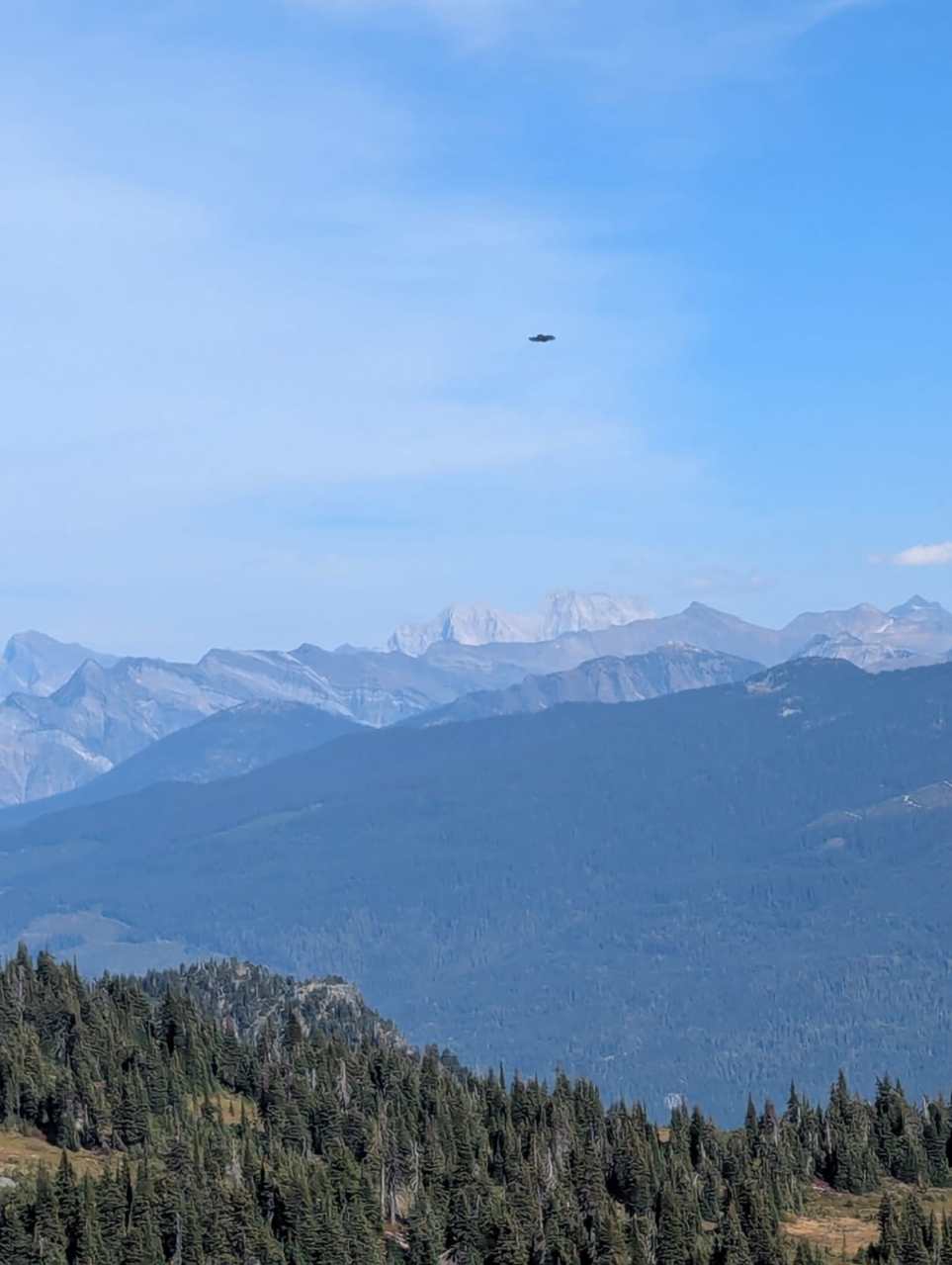 A distant view of a mountainous landscape with a blue sky and a flying object hovering in the distance.