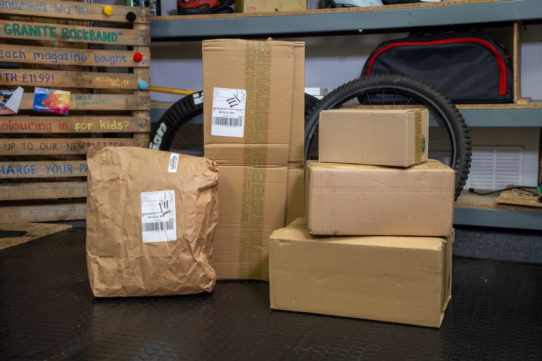 A collection of various packages in different sizes stacked on a textured floor, with a mountain bike tire visible in the background.