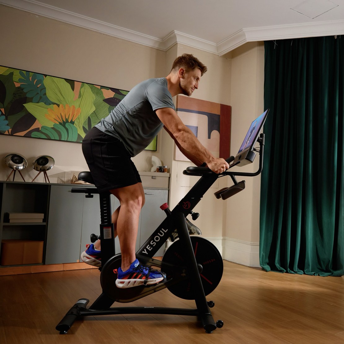 Person exercising on a Yesoul G1 M Plus indoor bike with a screen displaying workout content, set in a modern home environment.
