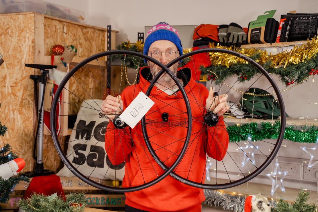 A person holding two HUNT Trail Wide MTB wheels in front of a festive, decorated background.