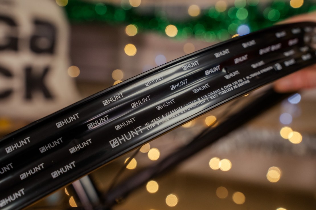 Close-up of a HUNT Trail Wide MTB wheel rim showcasing branding and specifications against a blurred festive background.