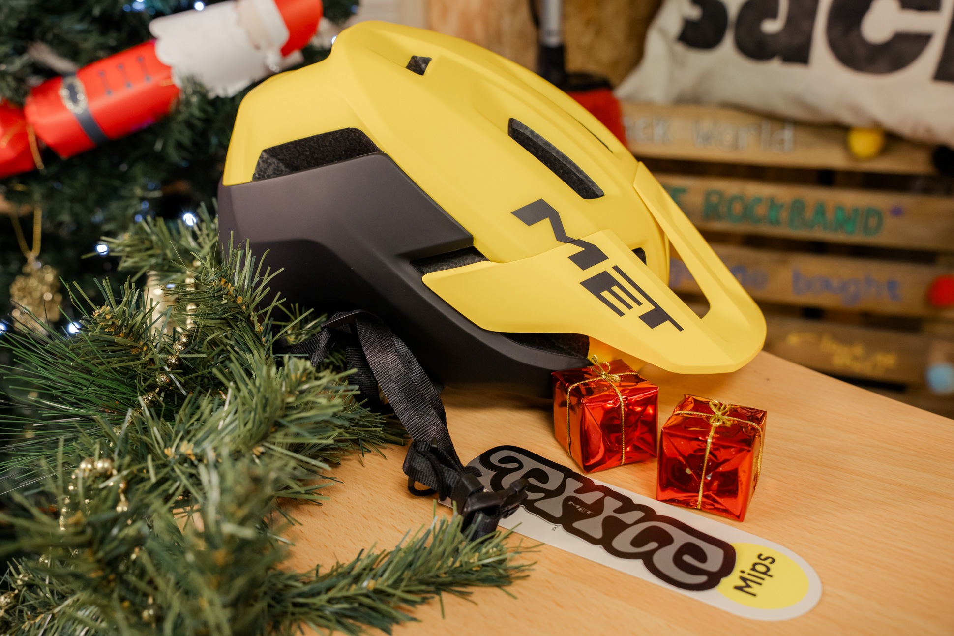 A yellow MET Terrae MIPS helmet displayed on a wooden surface surrounded by pine garlands, small red gift boxes, and festive decorations.