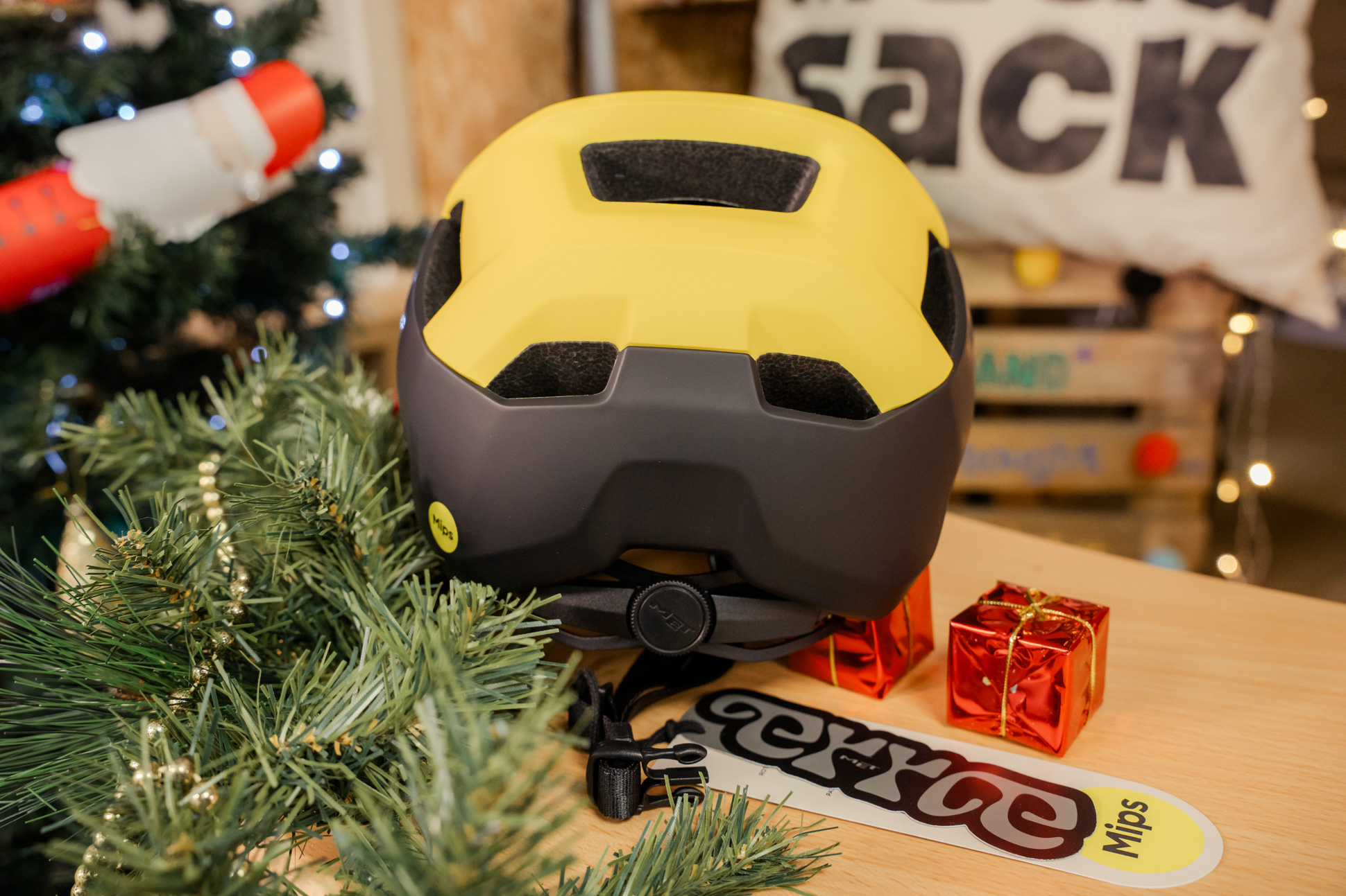 Back view of a MET Terrae MIPS helmet in black and yellow, placed on a wooden surface adorned with greenery and small red gift boxes.